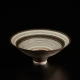Footed bowl by Lucie Rie, circa 1982, Porcelain, manganese glaze with concentric bands of sgraffito and inlaid design repeated inside and out, sold Dec 2024