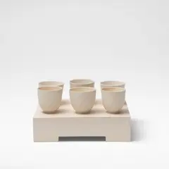 Julian Stair, Six cups on a ground, Porcelain, three examples in a matte glaze, three in a glossy white glaze, raised on a rectangular plaster composite ground