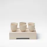 Julian Stair, Six cups on a ground, Porcelain, three examples in a matte glaze, three in a glossy white glaze, raised on a rectangular plaster composite ground