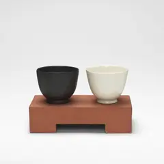 Julian Stair, Two Cups on a Ground, circa 2001, Porcelain, one example glazed in white, the other in matte black, raised on a rectangular terracotta ground
