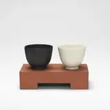 Julian Stair, Two Cups on a Ground, circa 2001, Porcelain, one example glazed in white, the other in matte black, raised on a rectangular terracotta ground