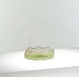 for James Couper & Sons by Christopher Dresser, circa 1895, Green glass, of shallow form with a folded rim, sold Mar 2025