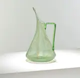 for James Couper & Sons by Christopher Dresser, circa 1895, Green glass, the conical body tapering to a pinched spout, set with an angled handle, offered Mar 2025