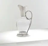 for James Dixon & Sons by Christopher Dresser, circa 1879, Clear glass with electroplated mounts, the bulbous body rising to a flared spout joined to the base by a curved handle, sold Mar 2025