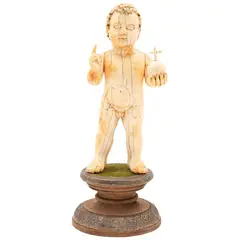 Niño Dios Salvador del Mundo, ORIGEN ORIENTAL, CA., 1900, Talla en marfil con detalles entintados, con peana de madera enchapada con lámina de plata repujada y cubierta de textil verde aterciopelado