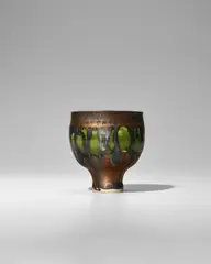 Small Footed Cup by Lucie Rie, porcelain, decorated with green glaze and a golden manganese running down the rim, impressed with artist's monogram, sold Jun 2025