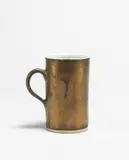 Mug by Lucie Rie, circa 1987, Stoneware, golden manganese glaze, shiny white glaze with green-hued band to the interior, sold Apr 2024