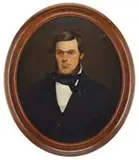 Unsigned, Portrait of a Belfast, Maine Merchant, Oval oil on canvas half portrait shows a young man with brown hair and brown beard wearing a black suit with white shirt