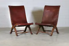 Pierre Lottier, Pair of Spanish leather low chairs, c.1950, each with a leather-upholstered curved seat and raised on 'X' frame supports united by stretchers