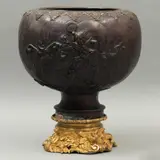 Macetero, JAPÓN, CA, 1900, Bronce, patinado en color marrón; decorado con relieves a manera de aves en enramada y representación de deidad con dragones; se incluye una base de bronce dorado con relieves de águilas y figuras florales (matrimonio)