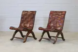 Pierre Lottier, Pair of Spanish leather low chairs, each with a leather-upholstered curved seat and raised on 'X' frame supports united by stretchers
