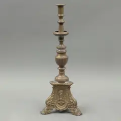 Candelero, CA., 1900, Bronce dorado, soporte trípode, fuste compuesto, decorado con relieves de imágenes religiosas y acantos