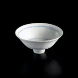 Footed bowl by Lucie Rie, circa 1978, Porcelain, matte white glaze with concentric inlaid blue lines repeated inside and out, sold Apr 2025