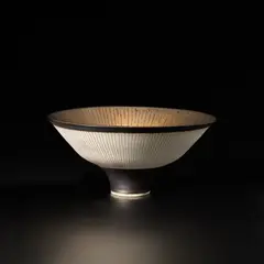 Footed bowl by Lucie Rie, circa 1980, Porcelain with golden manganese glaze, radiating inlaid and sgraffito design, sold May 2024