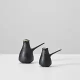 Lidded coffee pot and milk jug by Lucie Rie, circa 1955, Stoneware, the exterior with a manganese glaze and sgraffito design, the interior with white glaze, sold May 2024
