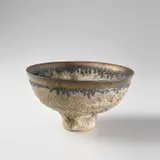 Footed bowl by Lucie Rie, circa 1986, Stoneware, volcanic grey glaze, golden manganese band around lip, sold May 2024