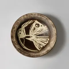 Large dish by Hans Coper, circa 1955, Stoneware, layered manganese glaze and white slip with a carved abstract bird design, beneath a clear glaze, sold Nov 2023