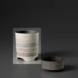 Cylindrical pot on tripod foot by Lucie Rie, circa 1958, Unglazed porcelain with bands of inlaid designs, the interior with a manganese glaze, sold Nov 2023