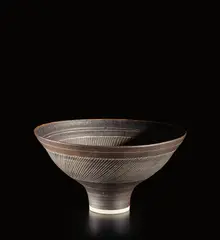 Footed bowl by Lucie Rie, circa 1970, Porcelain, manganese glaze with sgraffito design and blue glazed well, sold Mar 2019