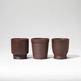 Three beakers by Keith Murray: Made by Wedgwood, circa 1935, Earthenware, brown basalt glaze, two of footed form (model no, sold Feb 2023
