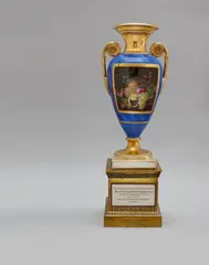 Königliche Porzellanmanufaktur Berlin Kpm, A large Berlin KPM porcelain vase with a fruit still life., On a fire-gilt bronze base inlaid with a porcelain plaque. Vase with rosette form handles, lapis blue ground with gilt veins, the front bearing a gilt framed rectangular reserve containing a finely painted still life after a Dutch design. The base with a relief palmette frieze, inscribed to the front “To the councilman and chamberlain of the capital and residential city of Berlin – Mr. Heinrich Friedrich Ludwig Falckeberg – on the day of 50th year of his service – the 17th July 1839. – The officers of the magistrate and the city deputations.” (from the German). Blue sceptre mark with KPM, red imperial orb mark. Some wear to the gilding of the bronze base. H of vase