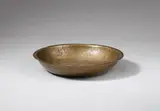 Probably German 12th century, A probably German 12th century bronze dish with engraved depictions of knights., With remains of gilding.. The dish is made of "tombak" bronze, which is copper mixed with a larger portion of tin, and belongs to a group of 11 similar dishes kept in various European collections, all of which have been published by Josepha Weitzmann-Fiedler (ibid.) in her seminal work on the subject. The centre is engraved with a six-pointed star surrounded by depictions of four knights dressed in chainmail, carrying shields and upraised swords, as well as four stylised palmtrees. With minor wear and rubbing