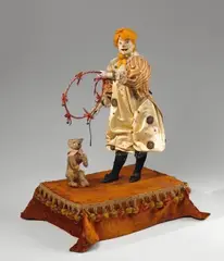 Léopold Lambert, A musical automaton formed as a clown taming a bear, Wind-up mechanism, firmly mounted original key and locking button. Painted wooden and papier mache head with glass eyes, metal tongue, porcelain hands, embroidered textile, fur and stuffing. The clown's arms and the bear's head move to the music. The key monogrammed LB. Labelled "LB La Rosière Modèle déposé" to the front of the socle. Label of the merchant "Au nain bleu E. Chauvière, Boul. des Capucines 27 Paris" to the underside. Soiled, the bear fur damaged, localised damage to the facial polychromy, wear to the velvet. H