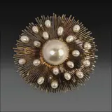 A Statement Pearl Brooch in 12k, Untitled, A 12k yellow gold brooch featuring a domed design with geometric rays bursting outward. At the center rests a Mabe pearl, surrounded by drop-shaped pearls and diamonds weighing approximately 0.21 carats.