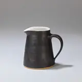 Lucie Rie, Small jug, circa 1958, Stoneware, manganese glaze to the exterior and handle, the interior with shiny white glaze