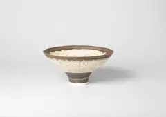 Dame Lucie Rie, A Footed Bowl, circa 1980, porcelain, incised sgraffito linear design in manganese against a cream glaze, highlighted with pale green bands