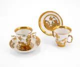 Zwei Doppelhenkelbecher mit Untertassen und überdekoriertem Drei-Freunde-Dekor by Meissen, Um 1725/30, Porzellan, blaue Unterglasur, gold überdekoriert und mit Achatstift radiert, sold Nov 2023