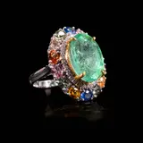 An Emerald Cocktail Ring in 18k, Untitled, The cocktail ring in 18k white gold is centered by an oval-shaped emerald weighing 10.90 cts. Vibrant multi-colored gems and diamonds encircle the center stone. <br><br> Weighs 10.30 grams. <br><br> Some stones noted as Refer on the GIA iD100®