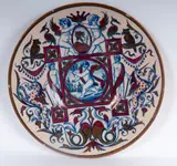 Paolo Rubboli, Polychrome ceramic pomp plate, Full-surface with a slight central recess. Decorated with cherubs and fantastic animals within frames and circular