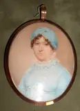Manner of John Comerford, A Lady, wearing blue dress with frilled white collar, her brown hair curled and upswept beneath a blue mob cap, oval yellow metal frame, the rear with the initial 'H' and plated hair, with applied paper label inscribed 'Samuel Shelley 1750-1808'