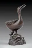 XVIIE SIÈCLE by Brûle-Parfum Chine - Dynastie Ming, Bronze à patine brune En forme de canard debout sur un rocher, la tête levée, le bec entro, sold Jun 2024