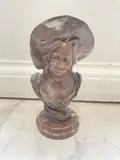 Buste de femme au chapeau by Victor Léopold Bruyneel, Épreuve en bronze à patine brune et verte sur une terrasse en marbre rouge, sold Dec 2021