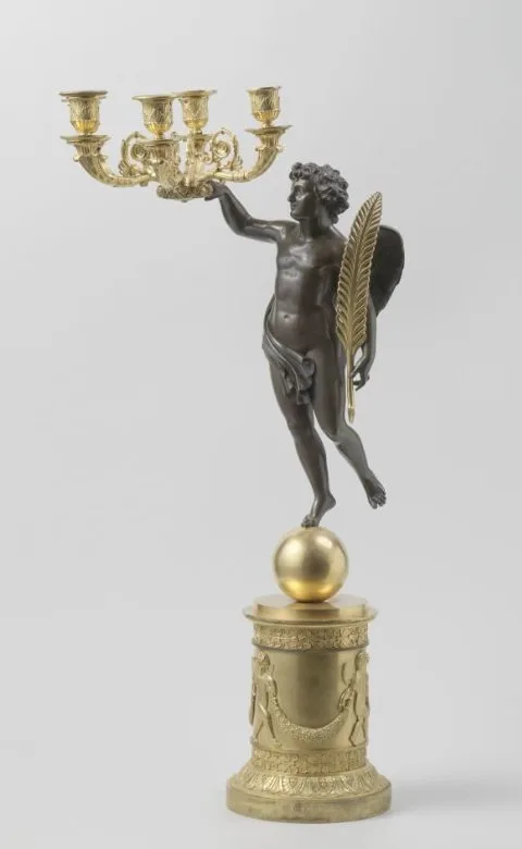 Pierre Philippe Thomire, Kandelaar van gedeeltelijk verguld brons, versierd met o.a. palmetten, gestileerde bloemranken, dansende putti met guirlande en een figuur in zweefstand met veer in de hand.