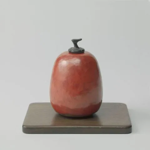 Henri Simmen, Pot, peervormig, met rode glazuur en een houten stopje, staande op een houten plankje